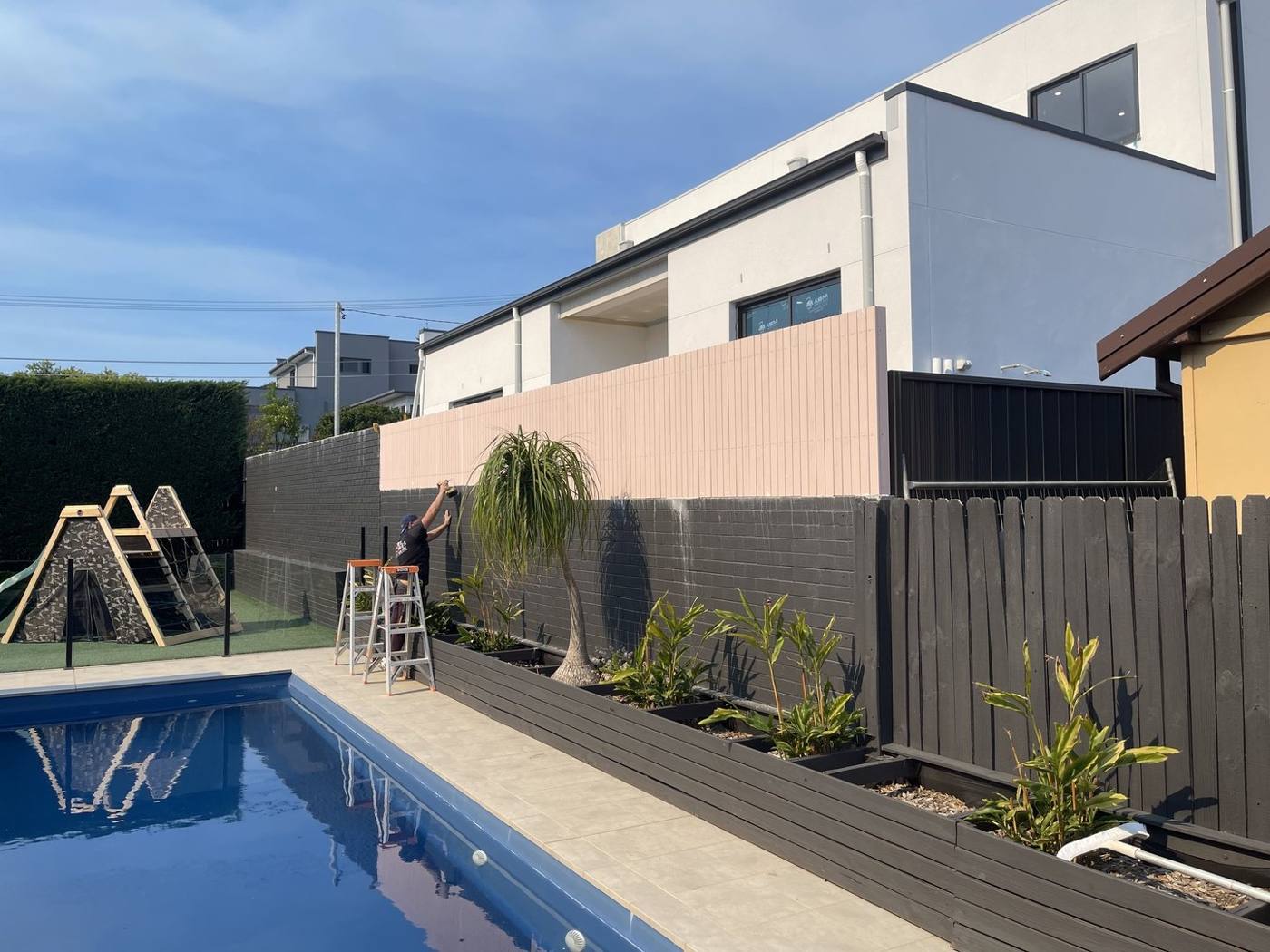 Pool with frameless glass fencing and black slat privacy screen by Loel Homes