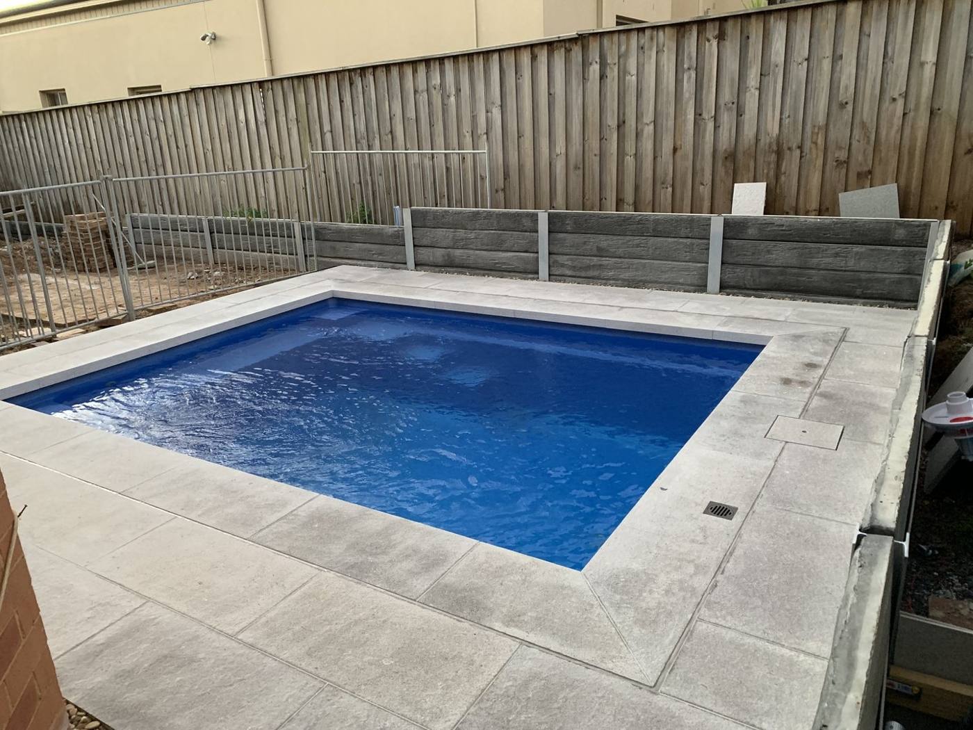 Finished square pool with grey coping and timber boundary fence by Loel Homes
