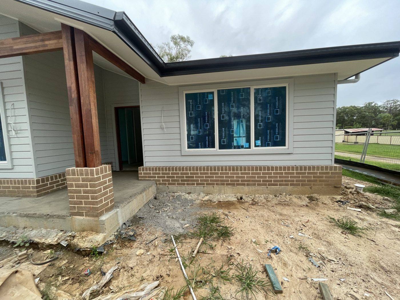 Finished front and side elevation with weatherboard cladding, timber posts and brick base, rural home by Loel Homes